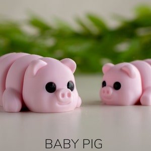 Puede incluir: Dos peque&ntilde;as figuras de cerditos rosas con ojos negros y caras sonrientes. Los cerdos est&aacute;n tumbados y el texto "BABY PIG" est&aacute; en la parte inferior de la imagen.
