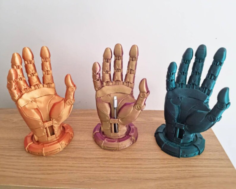 May include: Three 3D printed robot hand sculptures, each with a different color finish. The hands are posed with fingers extended and are mounted on a circular base. The colors are gold, purple, and teal.