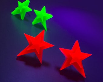 Può includere: Tre ornamenti a forma di stella, due sono verdi e uno è rosso. Gli ornamenti sono realizzati in un materiale lucido e sono disposti su una superficie di colore viola scuro.