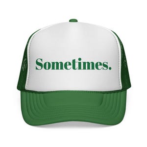 May include: A white and green trucker cap featuring a mesh back and a solid front panel. The word Sometimes. is printed in a dark green serif font across the centre of the white front panel. The brim and the mesh sides are a solid green colour.