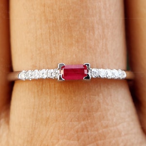 Könnte beinhalten: Ein zarter Silberring mit einem einzigen roten Rubin-Edelstein und einer Reihe kleiner Diamanten.