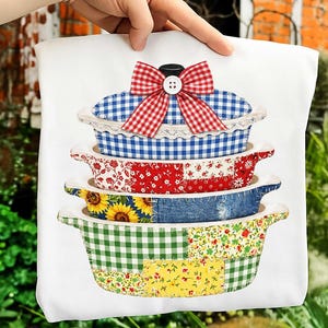Peut inclure: Sac fourre-tout blanc avec une pile de plats à gratin décoratifs. Le plat supérieur présente un motif vichy bleu et blanc avec un nœud rouge. Les autres plats ont des motifs floraux, de tournesols et de patchwork.