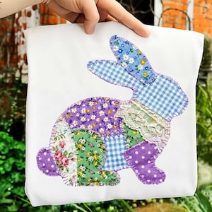 May include: White tote bag featuring a patchwork bunny design. The bunny is composed of various fabric patterns, including floral, gingham, and polka dots, in shades of blue, purple, green, and white. The bunny is stitched onto the bag with a contrasting thread.