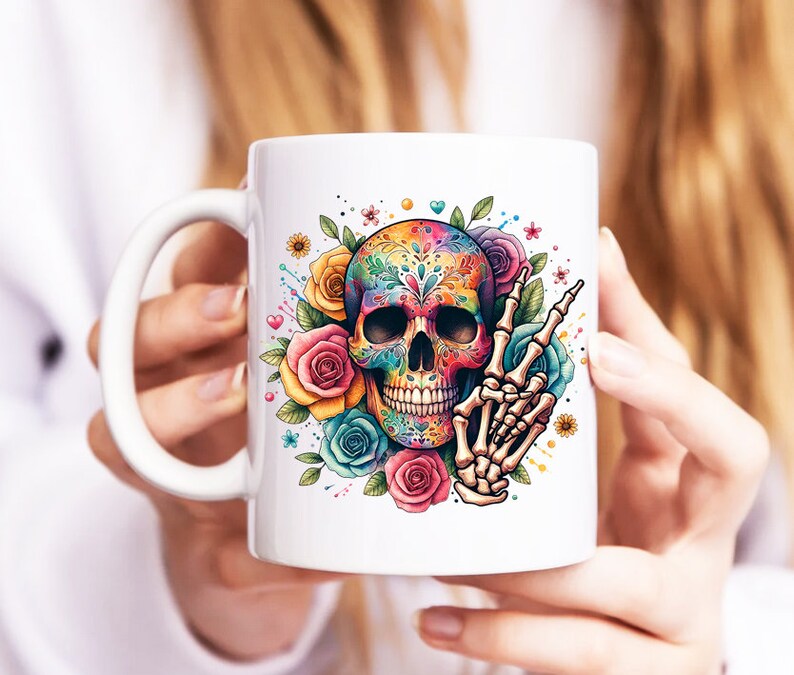 Peut inclure: Une tasse en c&eacute;ramique blanche avec un motif de cr&acirc;ne de sucre color&eacute;. Le cr&acirc;ne est d&eacute;cor&eacute; de fleurs et a un geste de main de signe de paix.