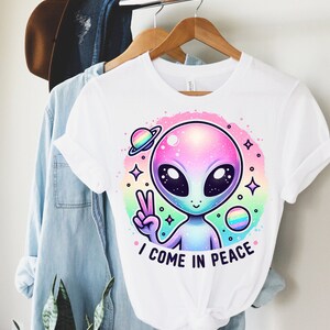 Puede incluir: Camiseta blanca con un gr&aacute;fico de extraterrestre arco&iacute;ris y el texto "Vengo en paz".
