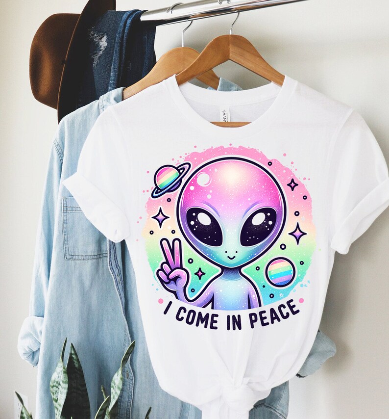 Puede incluir: Camiseta blanca con un gr&aacute;fico de extraterrestre arco&iacute;ris y el texto "Vengo en paz".