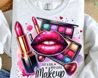 May include: A gray sweatshirt with a colorful graphic design featuring a pair of lips, lipstick, eyeshadow palettes, and a makeup brush. The text "Just a girl who loves makeup" is printed below the design.