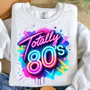 May include: A gray sweatshirt with a colorful graphic design of the text "Totally 80's" in a neon style. The design is surrounded by a pink, blue, and purple watercolor-like background.