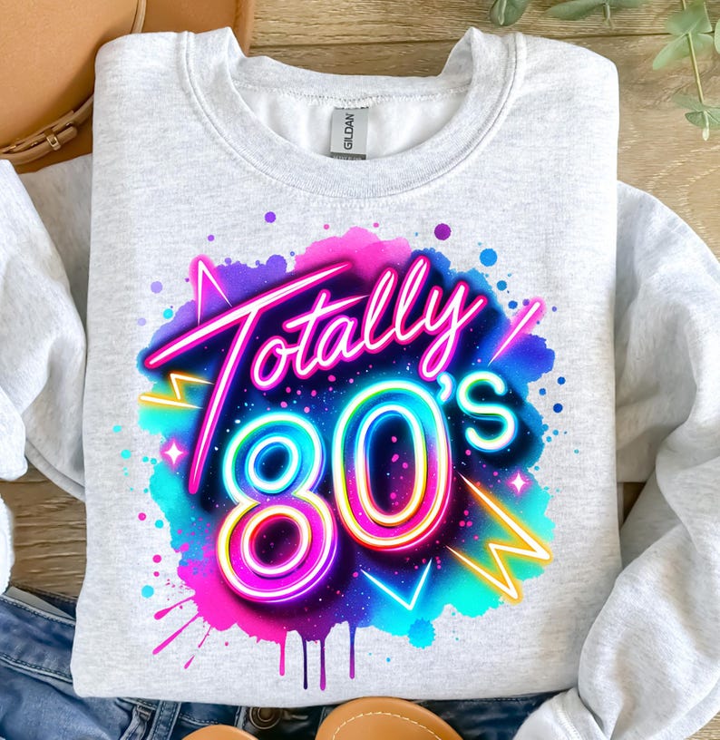 May include: A gray sweatshirt with a colorful graphic design of the text "Totally 80's" in a neon style. The design is surrounded by a pink, blue, and purple watercolor-like background.