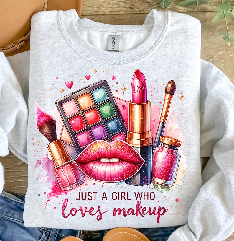 May include: A gray sweatshirt with a colorful graphic design of makeup items, including a lipstick, eyeshadow palette, and makeup brushes. The text "Just a girl who loves makeup" is printed below the graphic.