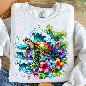 May include: A grey sweatshirt with a colorful graphic print of a sea turtle swimming in a wave with tropical flowers and leaves.