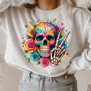 Peut inclure: Un sweat-shirt gris avec un motif de cr&acirc;ne de sucre color&eacute;. Le cr&acirc;ne est entour&eacute; de fleurs et a un signe de paix fait d'os.
