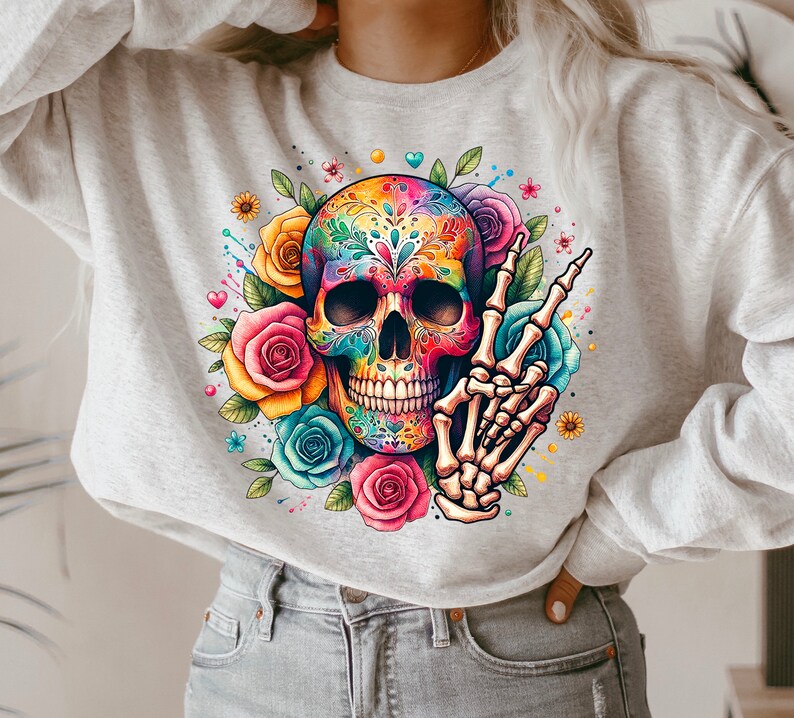 Peut inclure: Un sweat-shirt gris avec un motif de cr&acirc;ne de sucre color&eacute;. Le cr&acirc;ne est entour&eacute; de fleurs et a un signe de paix fait d'os.