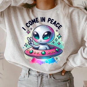 May include: A gray sweatshirt with a cartoon alien in a spaceship. The alien is waving with a peace sign and the text "I come in peace" is above the spaceship.