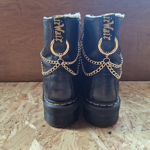 May include: Black leather ankle boots with gold chains and gold rings. The boots have the text "AirWair" on the back.