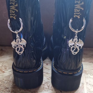 May include: Black leather boots with a platform sole and a silver dragon charm attached to each boot. The boots have a yellow tag that says "AirWair" on them.