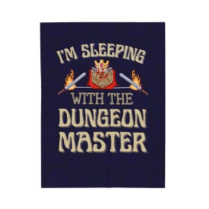 Puede incluir: Un fondo azul con el texto "I'm Sleeping With The Dungeon Master" en letras doradas. Una capa roja con una corona dorada y un dado de 20 caras está en el centro del texto.