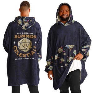 Op de afbeelding: Een marineblauwe hoodie-deken met een dobbelsteen en de tekst "Did someone summon celestials because here I am..." gedrukt op de voorkant. De achterkant van de deken is bedekt met een patroon van dobbelstenen en andere fantasy-themabeelden.