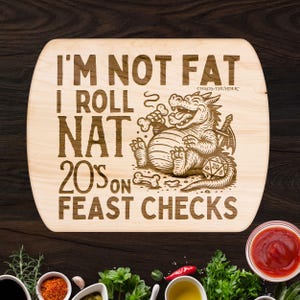 May include: A light-colored wooden cutting board with rounded edges, featuring engraved text and a cartoon dragon. The text reads "I'M NOT FAT I ROLL NAT 20'S ON FEAST CHECKS." A dice and bones are also engraved.