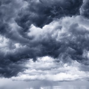 May include: A dark, stormy sky with heavy, gray clouds forming a dramatic, ominous pattern. The clouds are layered, with some appearing lighter and more wispy than others. The sky is mostly overcast, with only a few patches of blue visible. The horizon is obscured by the clouds, and the overall mood is one of impending rain.