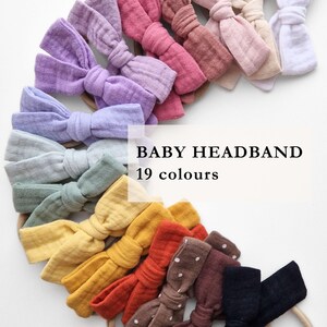 Pode incluir: Uma coleção de faixas de cabelo para bebês em várias cores, incluindo lavanda, rosa e amarelo. As faixas têm um design de laço e estão dispostas em semicírculo. O texto "BABY HEADBAND 19 colours" é exibido no centro.