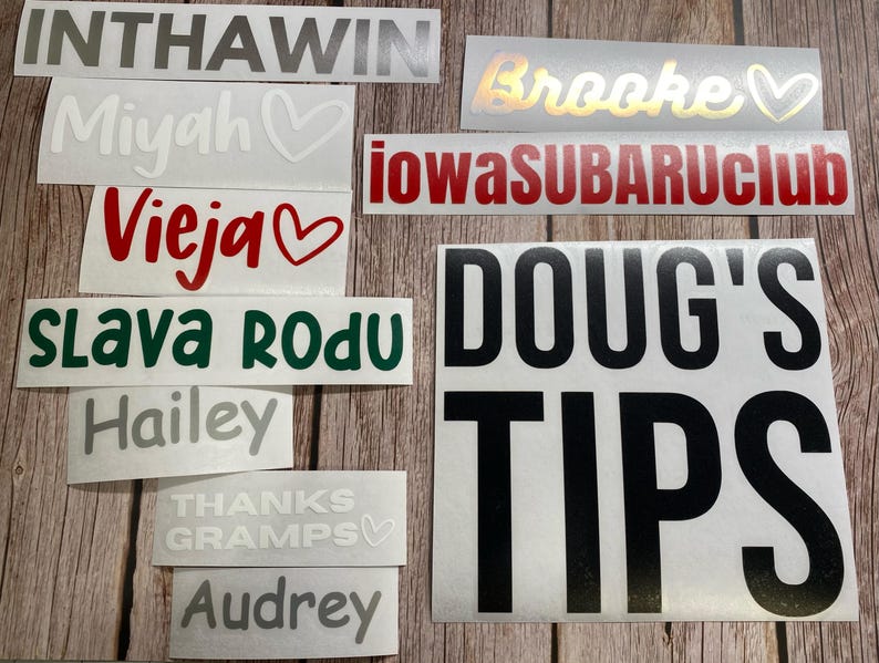 May include: A collection of various adhesive vinyl decals featuring text and heart symbols in different colors and fonts. The decals include the words INTHAWIN, Brooke, Miyah, iowaSUBARUclub, Vieja, SLAVA RODU, Hailey, THANKS GRAMPS, Audrey, and DOUG'S TIPS.