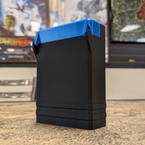May include: A black rectangular box with a blue top. The box has a textured surface and three raised bands around the bottom.