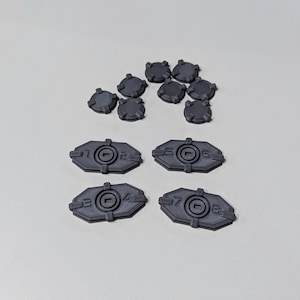 Op de afbeelding: Een set van acht grijze plastic spelstukken. Vier stukken zijn rond en vier stukken zijn rechthoekig. De rechthoekige stukken hebben de nummers 1-2, 3-4, 5-6 en 7-8 erop gedrukt.