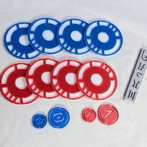May include: A set of red and blue game tokens with a white center. The tokens have a circular design with a raised edge. There are also two smaller red tokens with the number 7 printed on them. A gray plastic token with the word "DIE" printed on it is also included.