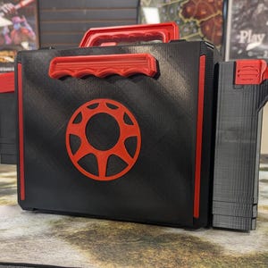 May include: Black and red 3D printed box with a red circular design on the front and a smaller black and red box attached to the right side. The box has a red handle on the top.