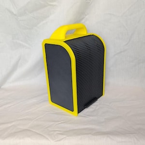 May include: A yellow and black portable speaker with a handle. The speaker has a rectangular shape with rounded corners. The front and back panels are black, while the edges and handle are bright yellow. The speaker has a black stand at the bottom.