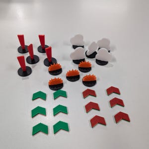 May include: A collection of colorful game pieces, including red and black posts, white cloud shapes, orange and black circular pieces, and green and red arrow shapes. The pieces are arranged on a white surface.