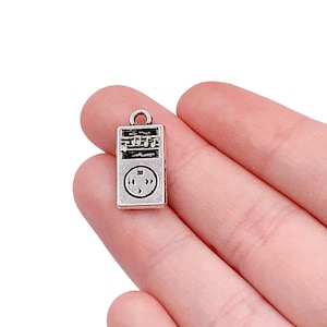 May include: Silver charm shaped like a music player with a black and white design. The charm has a loop at the top for attaching to a necklace or bracelet.