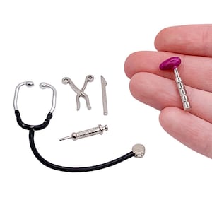 May include: A set of miniature medical tools, including a stethoscope, forceps, a scalpel, a syringe, and a reflex hammer. The tools are silver with black accents and the hammer has a purple head.