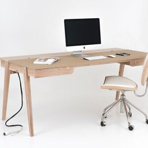 Puede incluir: Un escritorio de madera clara con un monitor de ordenador, teclado y ratón. Una silla blanca y beige con base cromada está junto al escritorio. El escritorio tiene un cajón y un cable de alimentación.