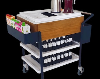 Puede incluir: Un carrito de bebidas móvil con un mueble de madera y bandejas blancas. Cuenta con un termo de acero inoxidable, una jarra de vidrio con líquido rojo y cajas de jugo. El carrito tiene varios estantes y ruedas.
