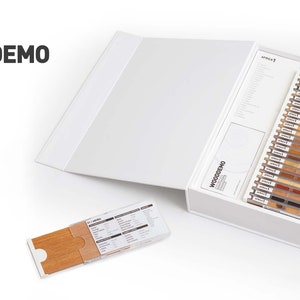 Op de afbeelding: Een witte doos met het label "WOODDEMO WORLDWIDE COMMERCIAL WOODS" met houten monsters. De set bevat een boekje en een display van verschillende houtstalen in verschillende kleuren en nerven. De doos is open.