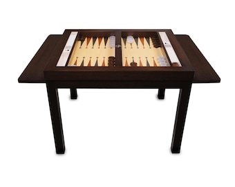 May include: A dark brown backgammon table with a light tan playing surface. The table has a built-in game board with brown and white game pieces. The table is rectangular with four legs and two side extensions.