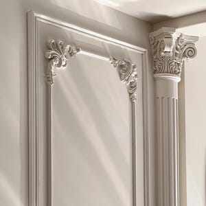 Op de afbeelding: Witte sierlijsten met een decoratief, gesneden ontwerp. De lijst maakt deel uit van een groter architectonisch element, mogelijk een deur of een boog.