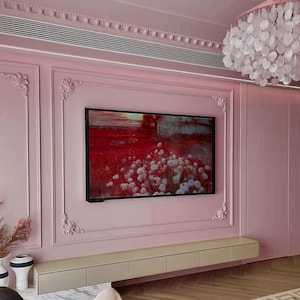 May include: A pink wall with ornate molding and a flat screen TV displaying a landscape painting. The TV is mounted above a long, white entertainment console with drawers.
