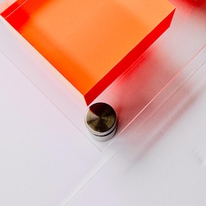 May include: A close-up of a clear acrylic frame with a bright orange square inside. A silver metal stand is attached to the bottom of the frame.