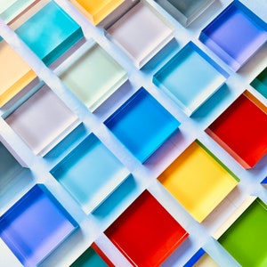 May include: A white background with various coloured squares arranged in a pattern. The squares are made of glass or plastic and have a glossy finish. The colours include blue, red, yellow, green, and white.