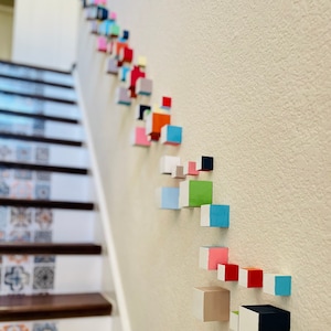 May include: A wall decorated with a colorful geometric pattern made of small wooden blocks. The blocks are arranged in a diagonal line, starting at the top left corner of the image and extending down to the bottom right corner. The blocks are painted in various colors, including red, blue, green, yellow, and orange.