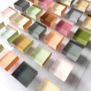 Pode incluir: Uma matriz de blocos quadrados transl&uacute;cidos e coloridos em v&aacute;rios tons de verde, rosa, laranja e cinza. Os blocos est&atilde;o dispostos em um padr&atilde;o de grade, criando uma exibi&ccedil;&atilde;o visualmente atraente. Os blocos parecem ser feitos de um material transparente.