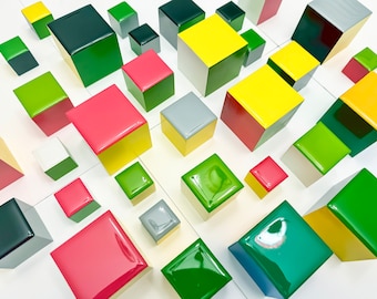 May include: A collection of colorful wooden blocks in various shades of green, red, yellow, and gray. The blocks are arranged in a grid pattern on a white surface.