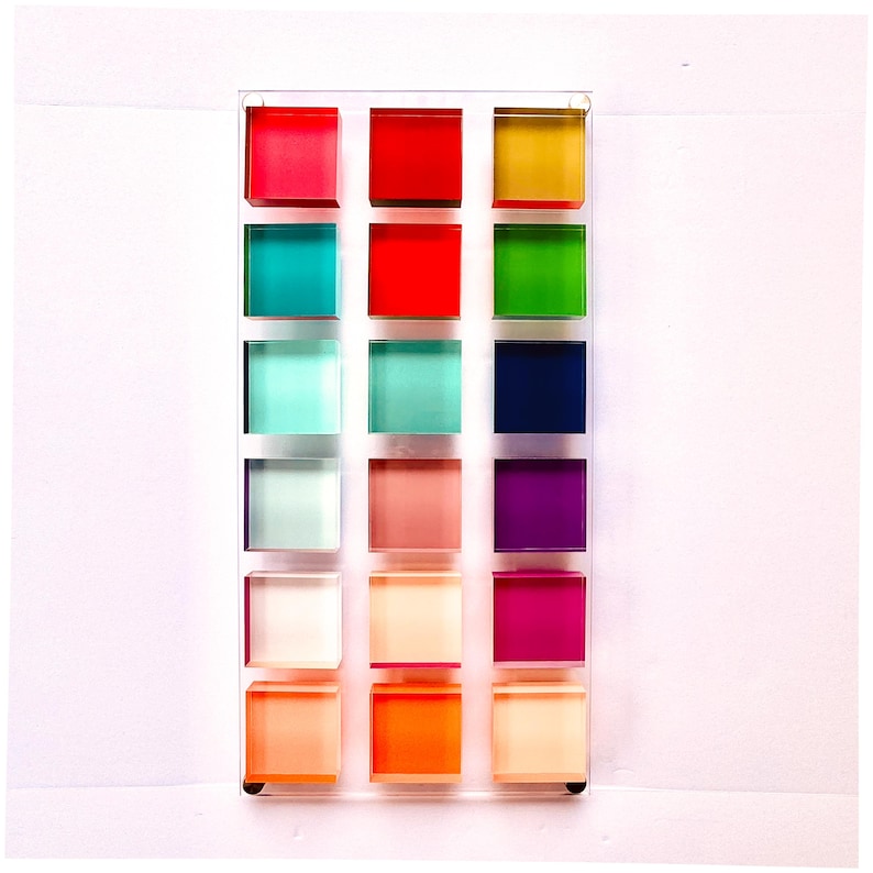 May include: A wall art piece with 18 colorful squares arranged in a grid. The squares are made of acrylic and are translucent, allowing light to shine through. The colors are vibrant and include red, orange, yellow, green, blue, purple, pink, and white.