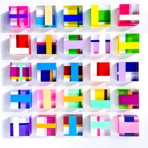 May include: Twenty-five clear acrylic cubes with colorful geometric designs. Each cube features a unique combination of bright colors, including pink, blue, yellow, green, and red. The cubes are arranged in a grid pattern against a white background.