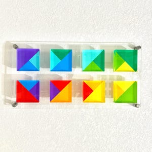 May include: A set of eight colorful geometric squares, each made of four triangles in different colors. The squares are arranged in two rows of four, with the colors alternating in a rainbow pattern.