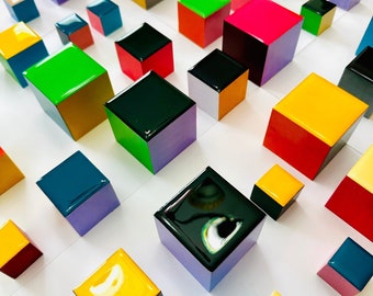 Puede incluir: Una colección de cubos de madera coloridos y brillantes dispuestos en un patrón de cuadrícula sobre una superficie blanca. Los cubos son de varios tamaños y colores, incluyendo rojo, amarillo, verde, azul, negro y morado.