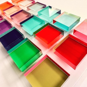 May include: A collection of colorful, square, acrylic blocks stacked on top of each other. The blocks are arranged in a staggered pattern, creating a visually appealing display. The colors include red, green, blue, purple, pink, and yellow.